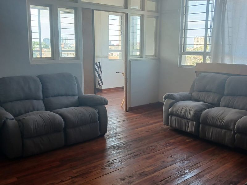 A living room featuring original hardwood flooring, large casement windows with transom detailing, and a central ceiling light fixture.