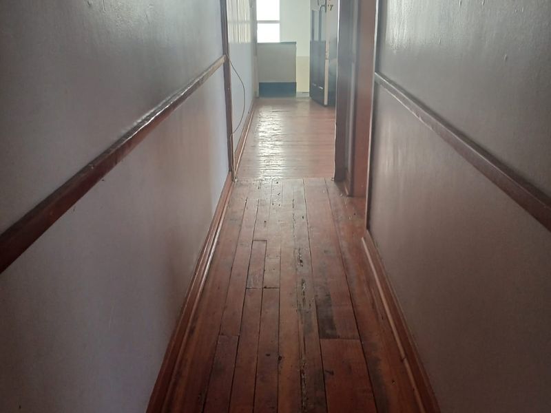 A narrow hallway featuring original timber flooring and timber dado rails, leading towards an entrance area with natural light.