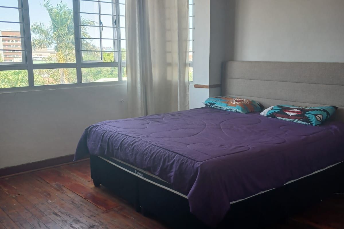 A bedroom featuring original timber flooring, large windows with security bars, and neutral wall finishes.