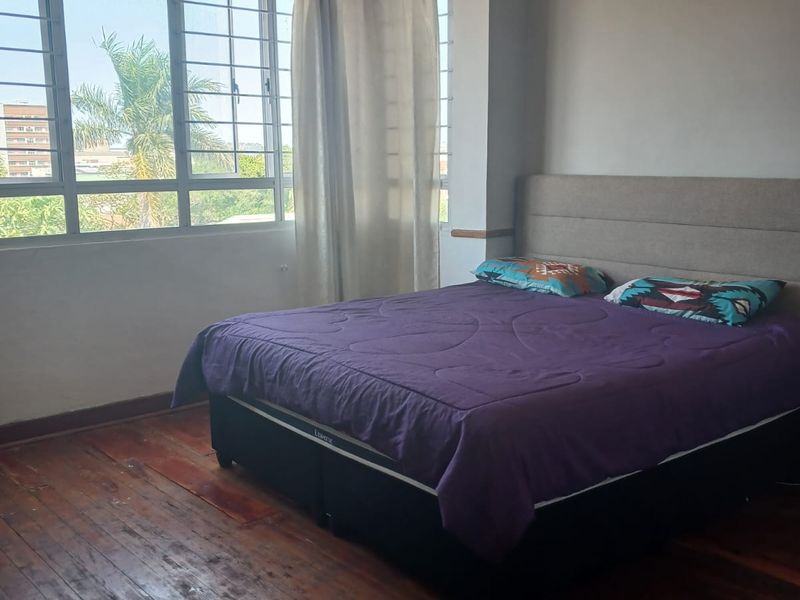 A bedroom featuring original timber flooring, large windows with security bars, and neutral wall finishes.