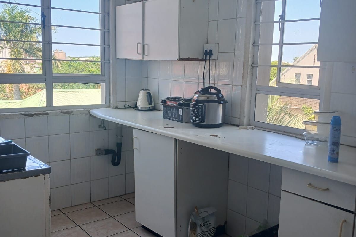 A functional kitchen featuring tiled surfaces, built-in cabinetry, and ample natural light through large windows with security bars.