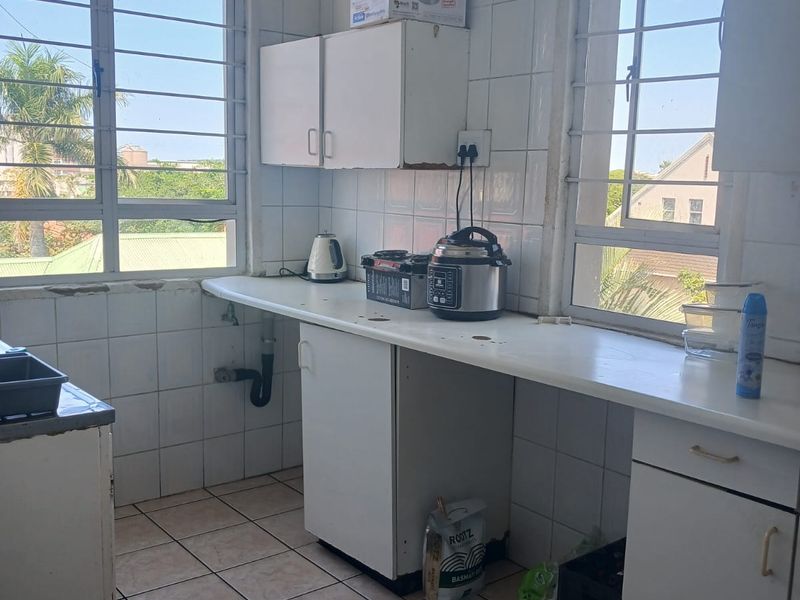 A functional kitchen featuring tiled surfaces, built-in cabinetry, and ample natural light through large windows with security bars.