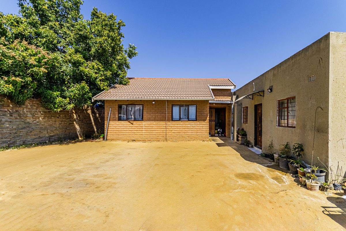 Rear view of the property featuring a face brick facade, tiled roof, and a large concrete courtyard area.