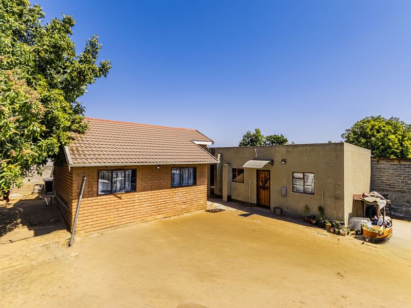 Rear view of the property featuring a face brick structure with a tiled roof and an adjacent plastered building with a large unpaved yard.