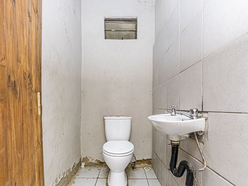 A compact bathroom featuring a wall-mounted basin and toilet, requiring cosmetic updates and repairs to the wall finishes and plumbing fixtures.