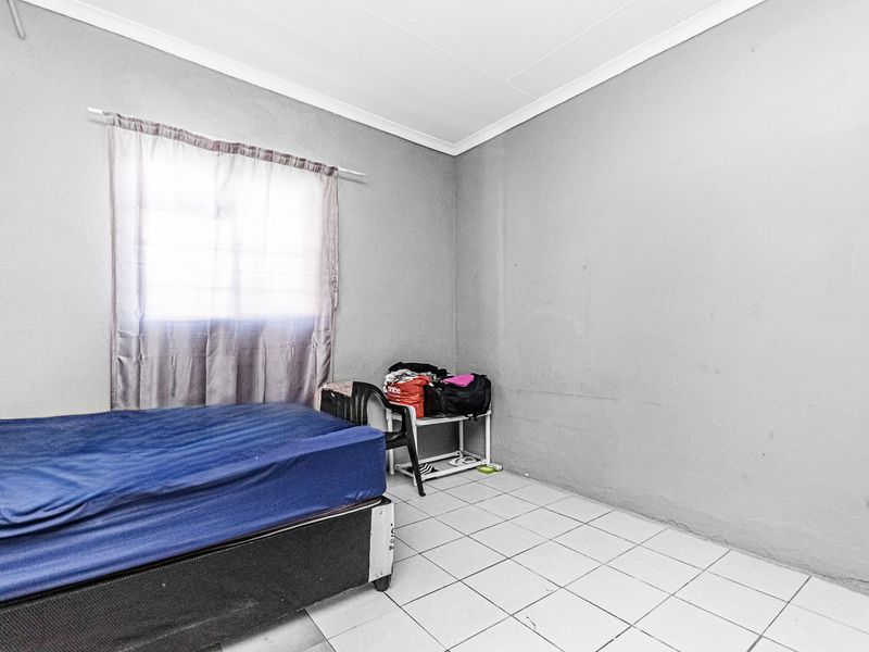 A simple bedroom featuring tiled flooring and neutral grey walls, offering a blank canvas for potential interior updates.