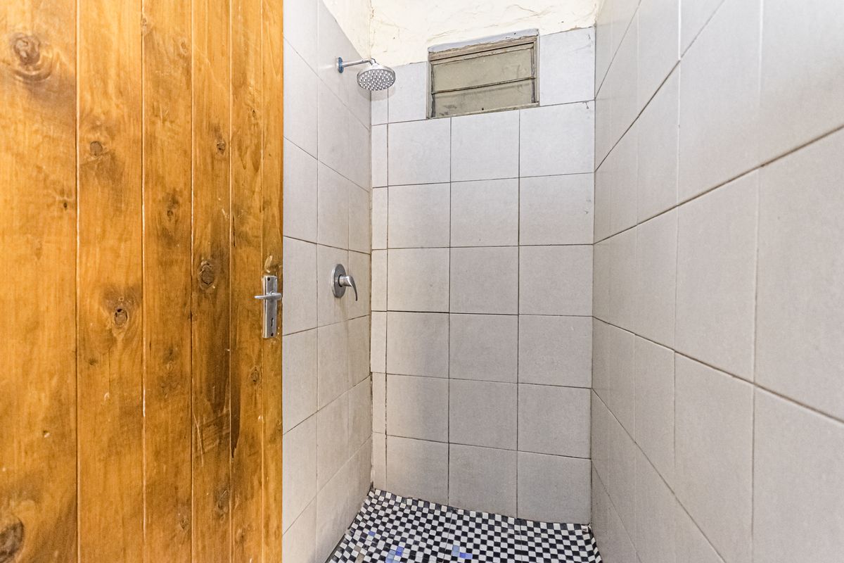 A compact shower enclosure featuring tiled walls, a checkered floor, and a wooden door, requiring some cosmetic updates to the ceiling and finishes.