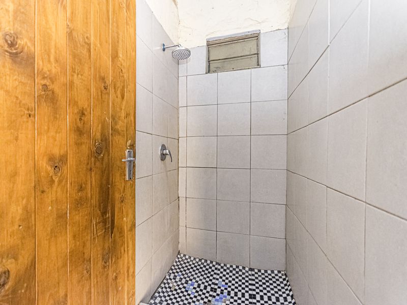 A compact shower enclosure featuring tiled walls, a checkered floor, and a wooden door, requiring some cosmetic updates to the ceiling and finishes.