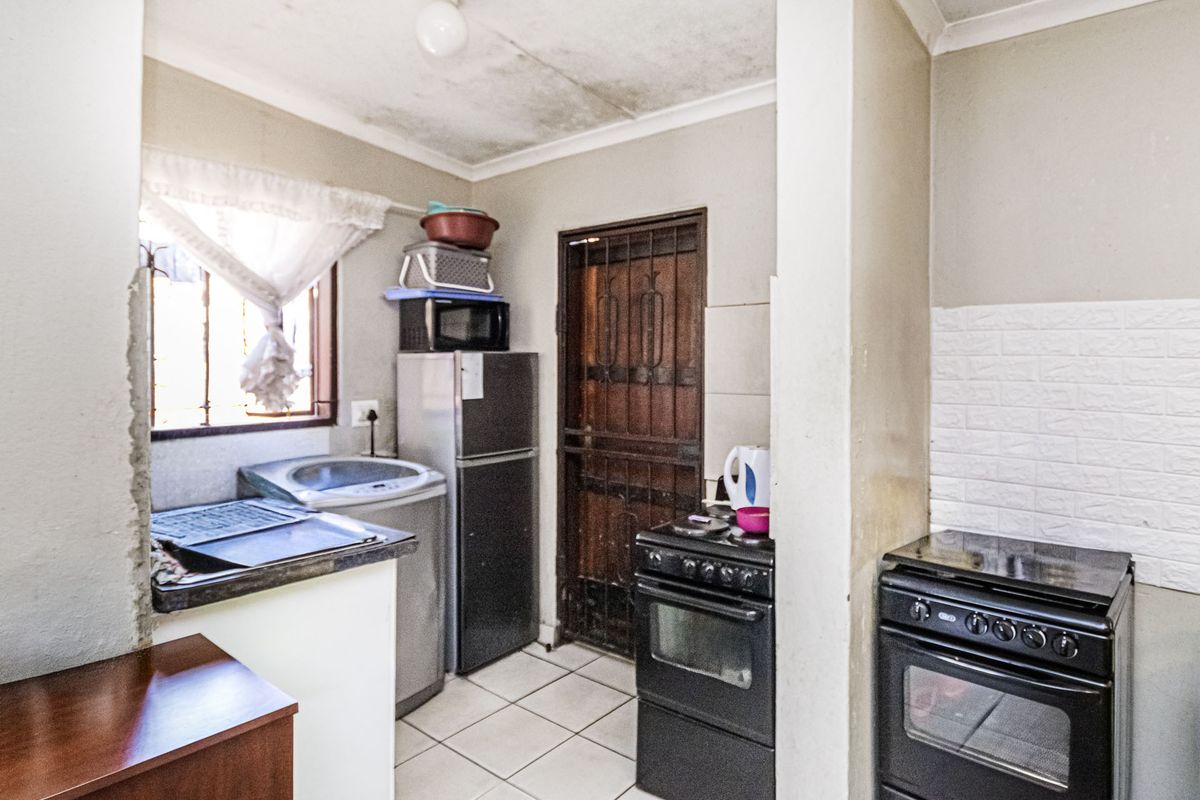 Compact kitchen area featuring tiled flooring, a security gate, and built-in cooking appliances, requiring maintenance to the ceiling and wall finishes.