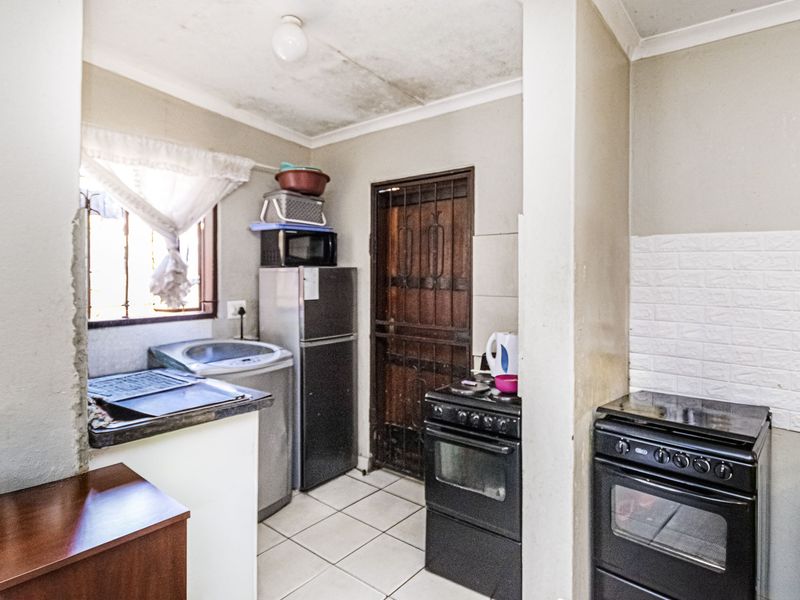 Compact kitchen area featuring tiled flooring, a security gate, and built-in cooking appliances, requiring maintenance to the ceiling and wall finishes.