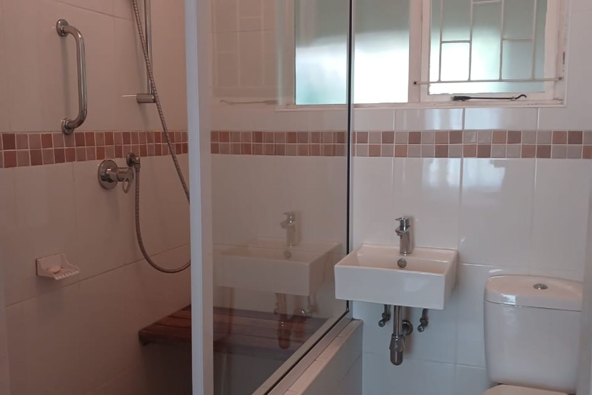 A functional bathroom featuring a walk-in shower with a glass screen, wall-mounted basin, and toilet, finished with neutral wall and floor tiles.