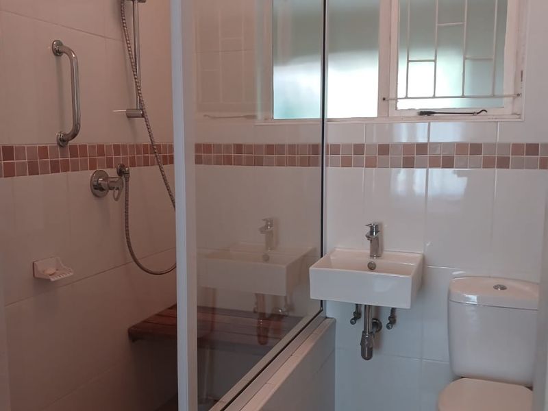 A functional bathroom featuring a walk-in shower with a glass screen, wall-mounted basin, and toilet, finished with neutral wall and floor tiles.