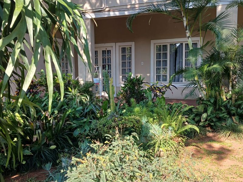 A rear view of the apartment featuring a covered patio area, french doors, and security gates, surrounded by a lush garden.