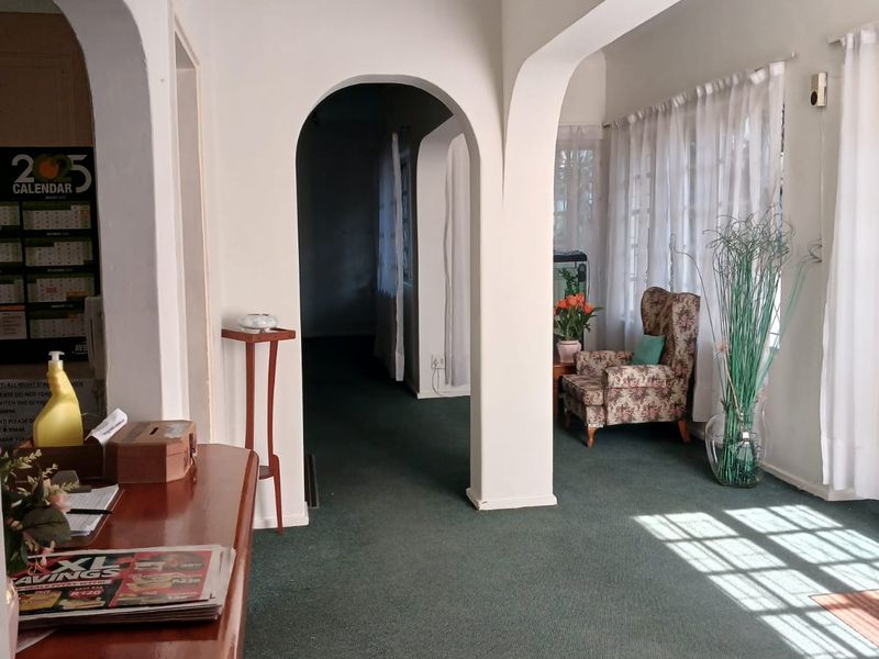A living area featuring distinctive architectural archways, large windows allowing natural light, and carpeted flooring throughout the space.