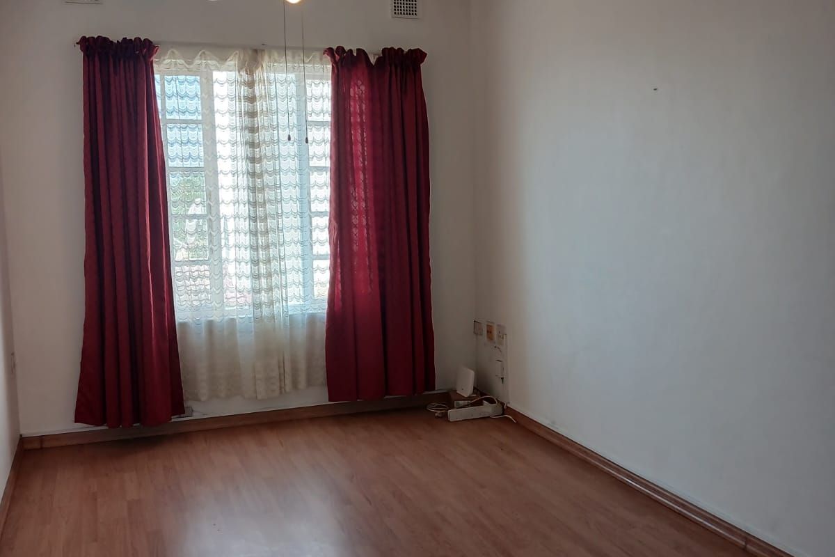 A spacious, empty bedroom featuring laminate flooring, a ceiling fan, and natural light through a window with existing curtain fixtures.