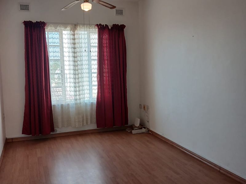 A spacious, empty bedroom featuring laminate flooring, a ceiling fan, and natural light through a window with existing curtain fixtures.