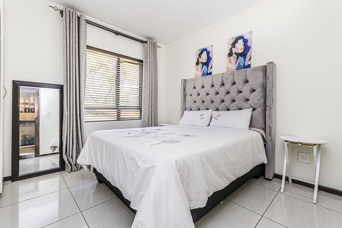 A well-maintained bedroom featuring neutral tiled flooring, large window with venetian blinds, and modern curtain rails.