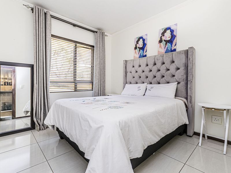 A well-maintained bedroom featuring neutral tiled flooring, large window with venetian blinds, and modern curtain rails.