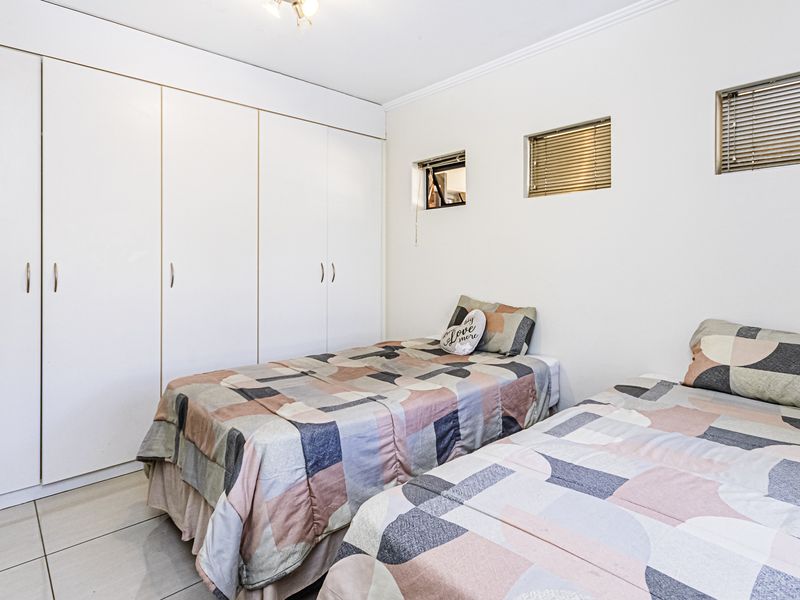 A bedroom featuring built-in cupboards, tiled flooring, and small windows with fitted venetian blinds.