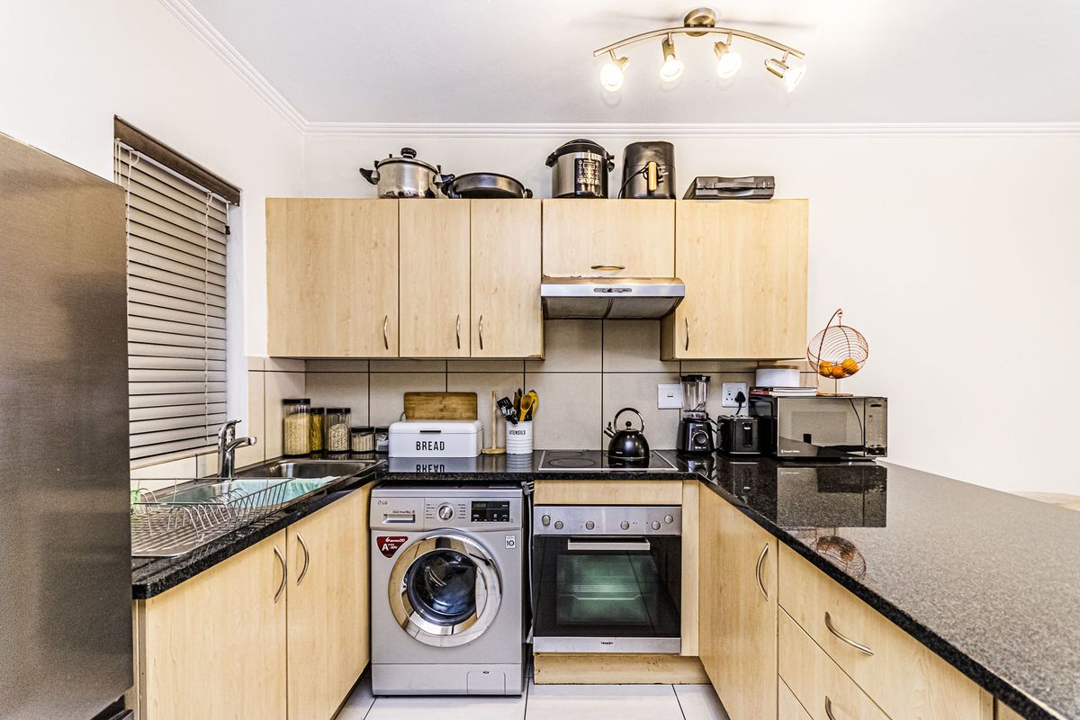 Compact kitchen featuring light wood cabinetry, granite countertops, built-in oven, electric hob, extractor fan, and an integrated washing machine.