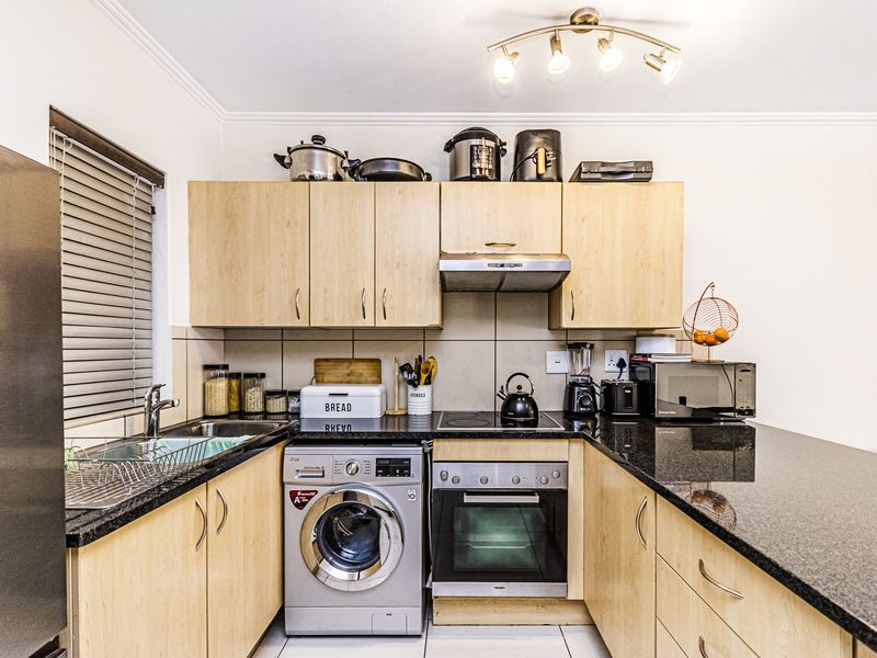 Compact kitchen featuring light wood cabinetry, granite countertops, built-in oven, electric hob, extractor fan, and an integrated washing machine.