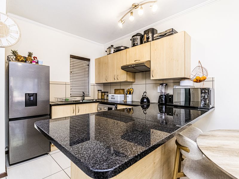 A functional kitchen featuring granite countertops, light wood-finish cabinetry, a tiled backsplash, and a breakfast bar area.