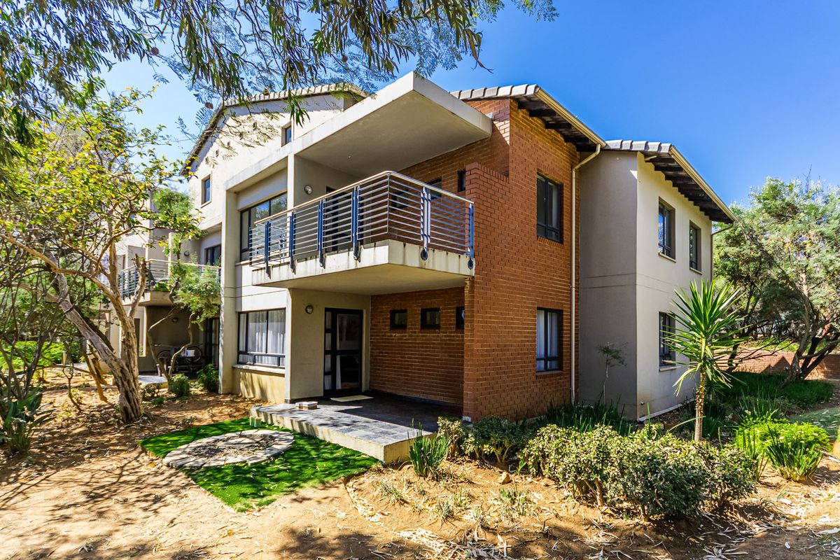 Rear view of a multi-story apartment building featuring a private balcony, ground floor patio, and a combination of brick and rendered exterior finishes.