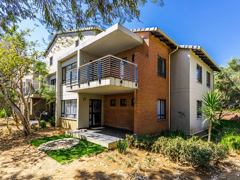 Rear view of a multi-story apartment building featuring a private balcony, ground floor patio, and a combination of brick and rendered exterior finishes.