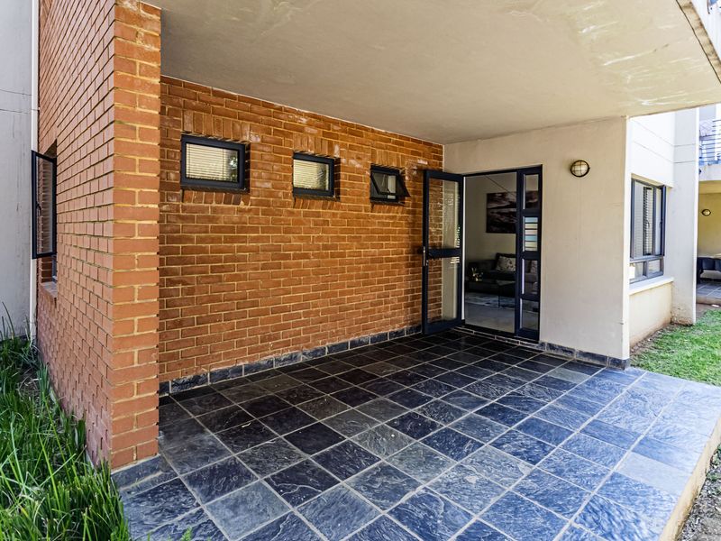 A covered patio area featuring exposed brickwork, dark tiled flooring, and direct access to the interior living space through a glass door.
