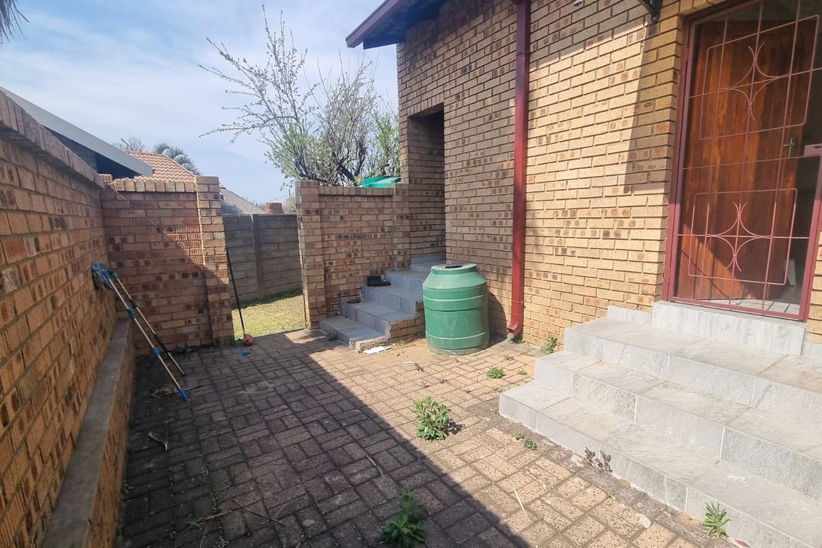 A rear courtyard area featuring brick boundary walls, paved flooring, and concrete steps leading to a secure entrance.