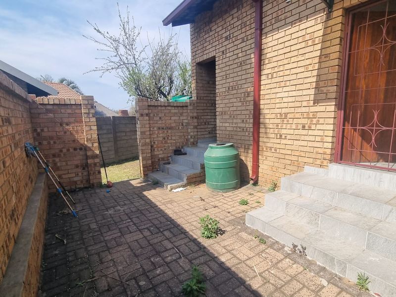 A rear courtyard area featuring brick boundary walls, paved flooring, and concrete steps leading to a secure entrance.