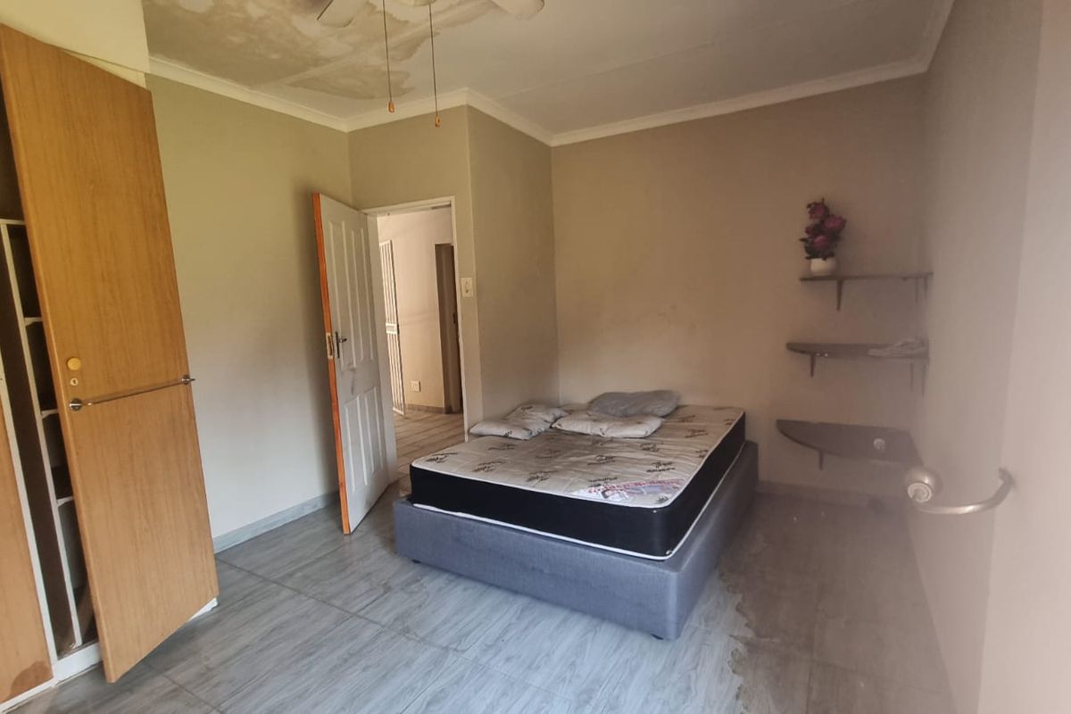 A bedroom featuring tiled flooring, a built-in wardrobe, and wall-mounted shelving, showing signs of ceiling water damage and floor tile wear.