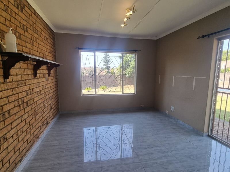 An empty living room featuring a prominent exposed brick wall, modern grey tiled flooring, and direct access to the garden through a security gate.