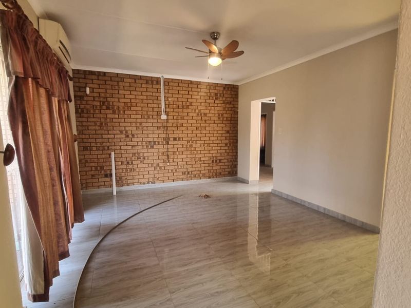 Spacious living area featuring an exposed brick accent wall, tiled flooring, and a ceiling fan, offering a versatile layout for comfortable family living.