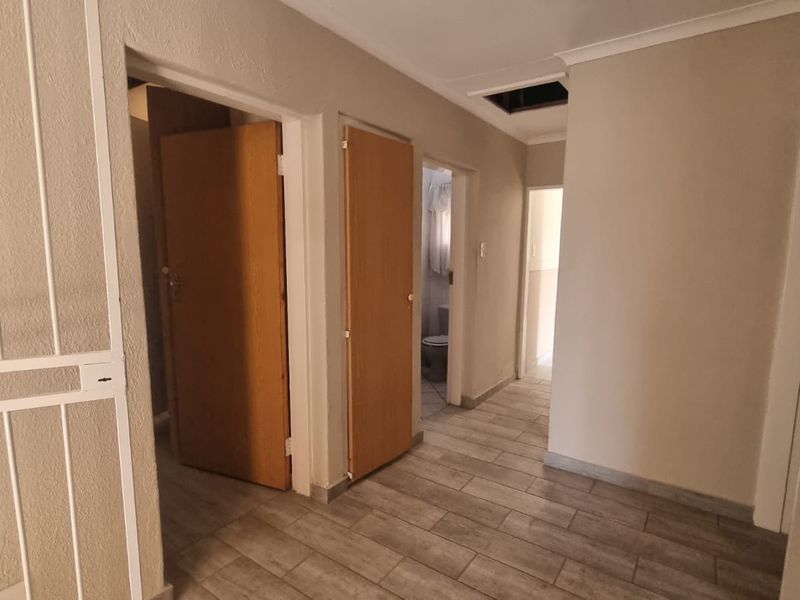 A functional hallway featuring tiled flooring, multiple internal access doors, and a ceiling loft hatch, providing central circulation throughout the home.