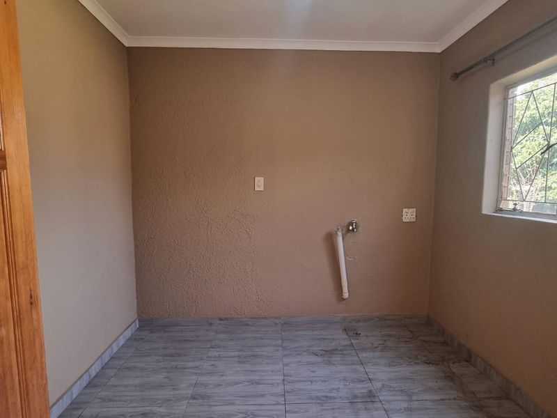A functional laundry room featuring tiled flooring, plumbing connections for appliances, and a window with security bars.