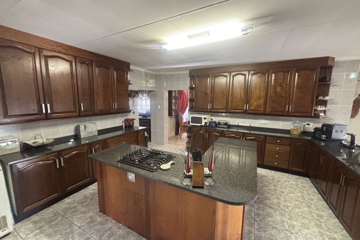 Spacious kitchen featuring dark wood cabinetry, granite countertops, a central island with a gas hob, and tiled flooring.