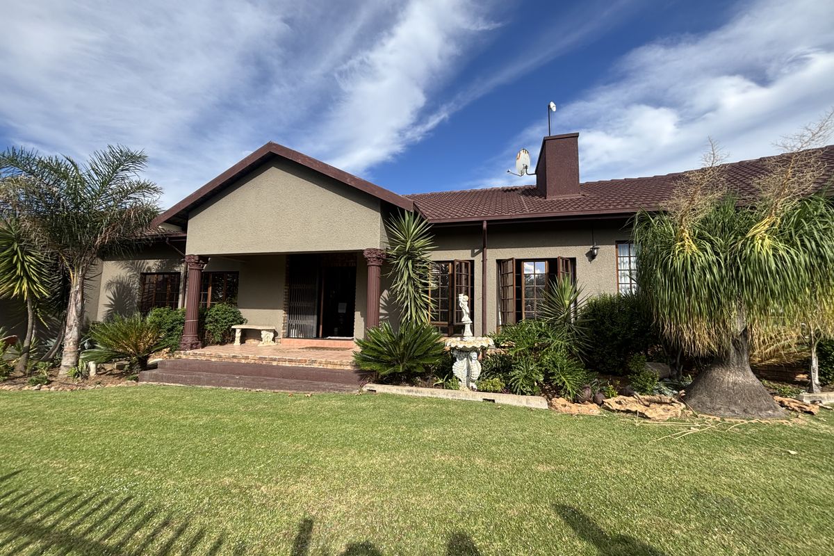 A well-maintained rear exterior view of the house featuring a covered patio, decorative columns, and a spacious landscaped garden.