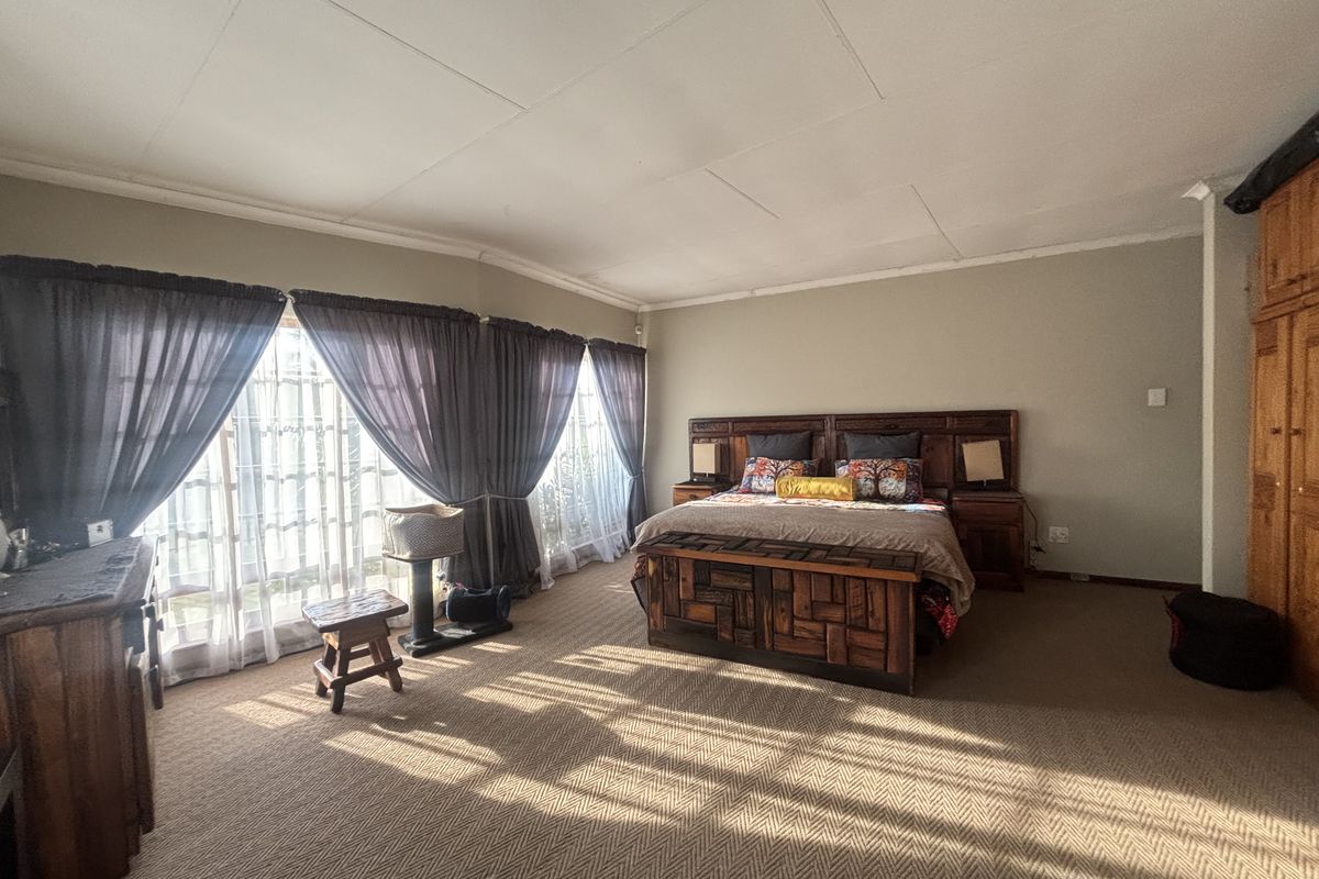 Spacious bedroom featuring carpeted flooring, built-in wooden cupboards, and large windows with natural light.