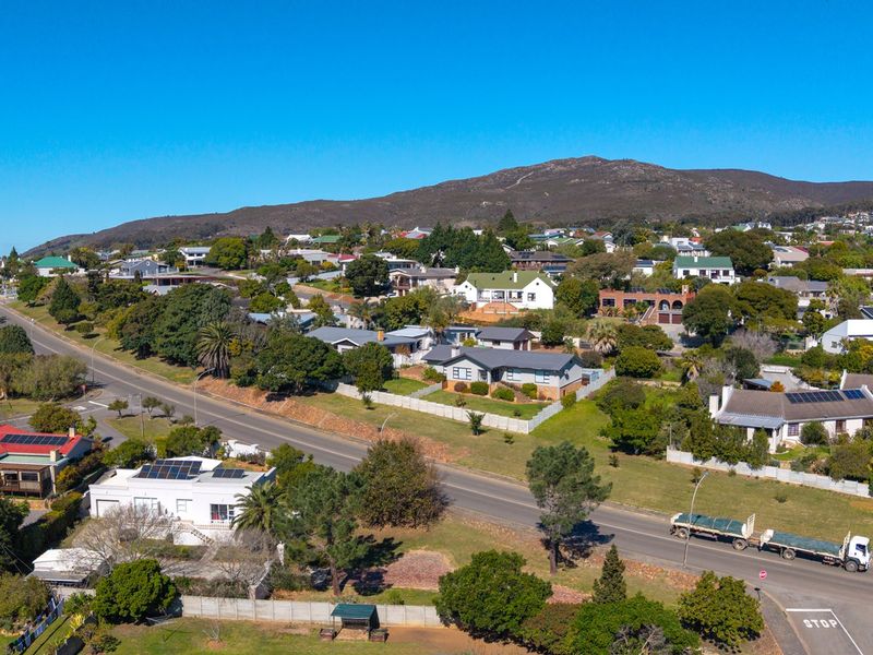 An aerial view of a residential neighborhood featuring established homes, mature trees, and a mountain backdrop under a clear blue sky.