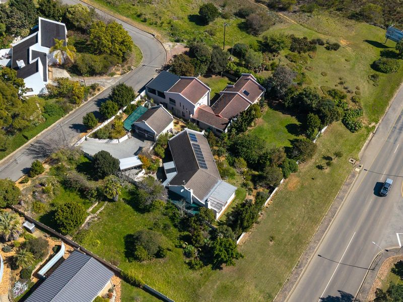 Aerial view of a residential property featuring multiple buildings, tiled roofs with solar panels, established gardens, and paved driveway access.