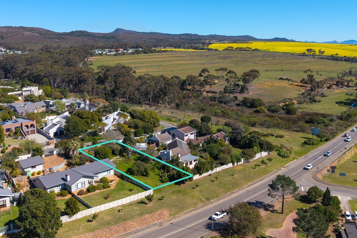 An aerial view of a vacant residential plot outlined in blue, situated in a suburban area with surrounding landscape and road access.