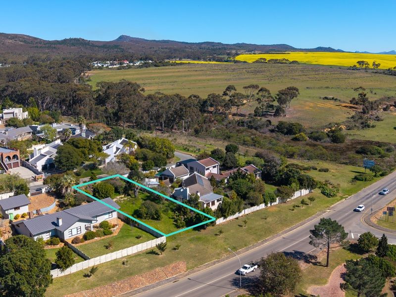 An aerial view of a vacant residential plot outlined in blue, situated in a suburban area with surrounding landscape and road access.