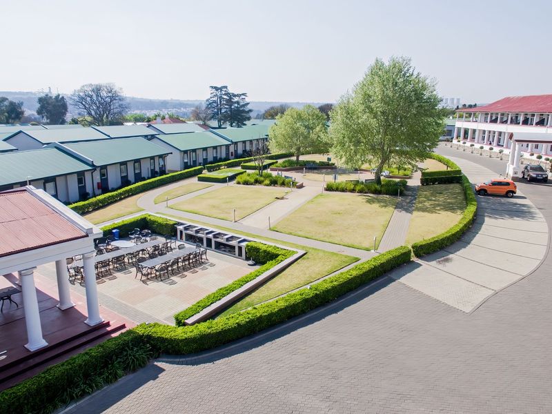 Aerial view of a well-maintained apartment complex featuring a central landscaped garden, paved driveway, and a covered patio area with built-in braai facilities.