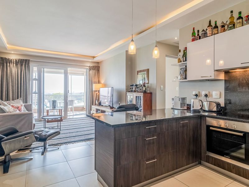 Modern open-plan living area featuring a sleek kitchen with granite countertops, built-in appliances, and seamless flow to a balcony with natural light.