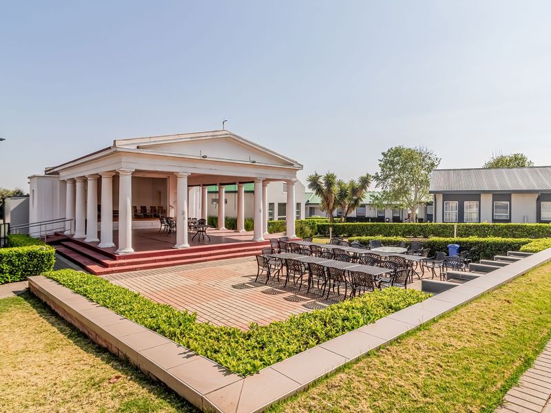 A well-maintained outdoor clubhouse area featuring a neoclassical pavilion with columns, a raised deck, and surrounding landscaped gardens.