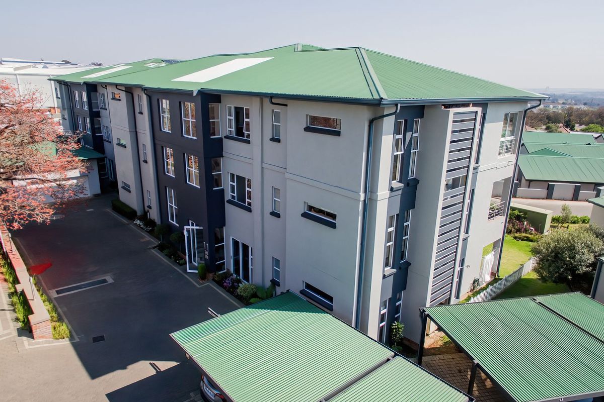 Aerial view of a modern multi-story apartment complex featuring a green corrugated metal roof, paved driveway, and dedicated carport parking areas.