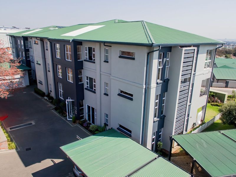Aerial view of a modern multi-story apartment complex featuring a green corrugated metal roof, paved driveway, and dedicated carport parking areas.