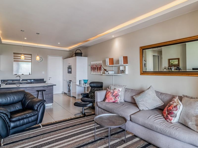 Spacious open-plan living area featuring a modern kitchen with integrated appliances, stone countertops, and elegant recessed cove lighting throughout the space.