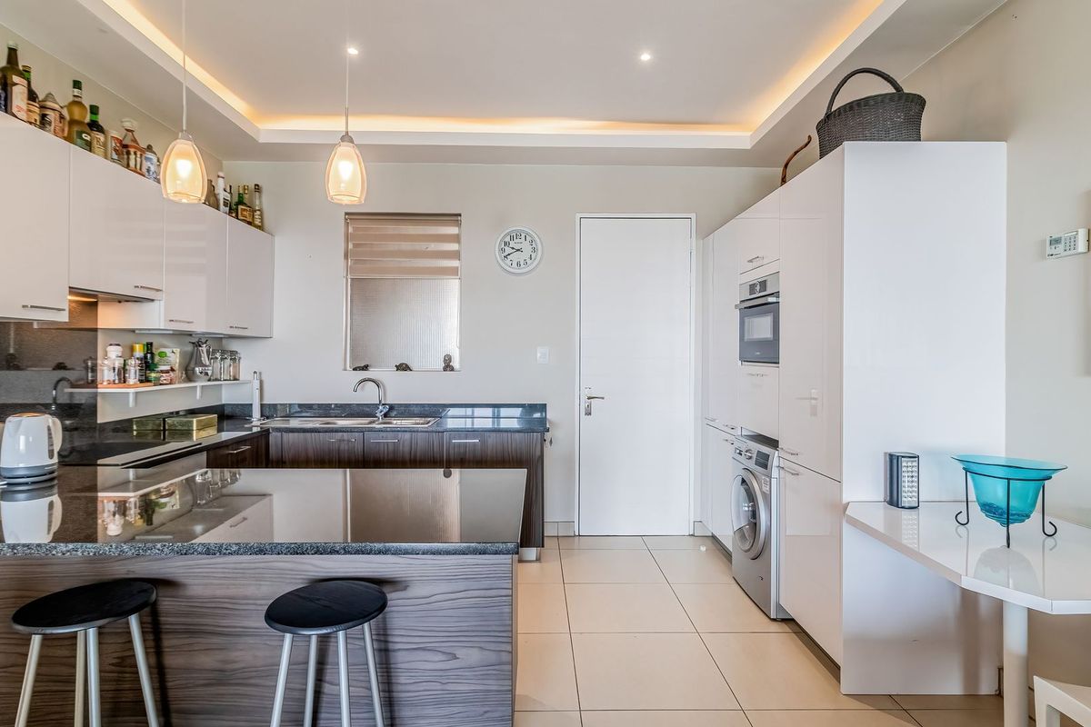 Modern kitchen featuring sleek white and wood-grain cabinetry, granite countertops, integrated appliances, and recessed ceiling lighting with a breakfast bar area.